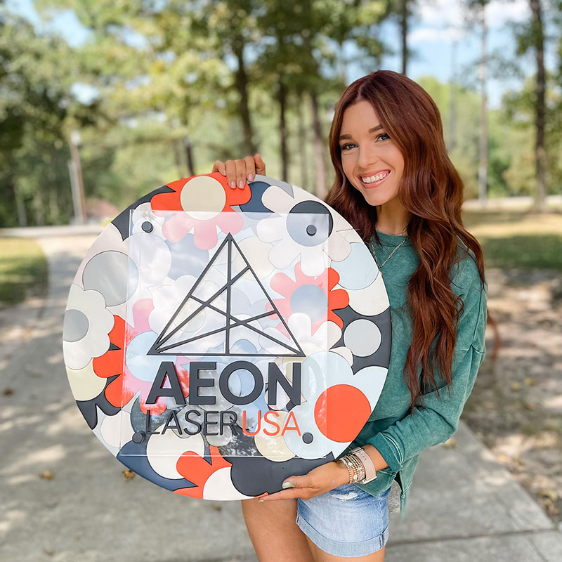photo of a women with wavy light brown hair, smiling and holding a custom made nursery round sign, in a natural outdoor setting