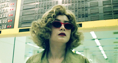 A close-up screenshot of a confident woman in sunglasses and a blonde wig looking off-camera. From the film 'Chungking Express'.