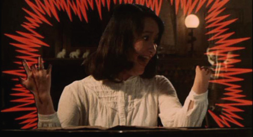 A screenshot of a girl named Melody (played by Eriko Tanaka) holding up her hands in shock at the loss of her fingers. Orange comic book style shock lines surround her. From the Japanese film 'House'.