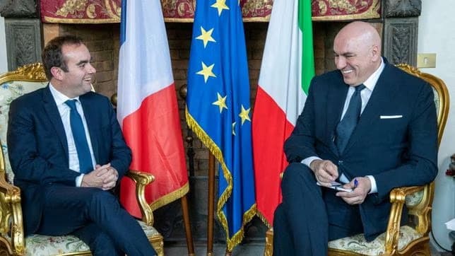 2 politicos sentados con la bandera italiana detras