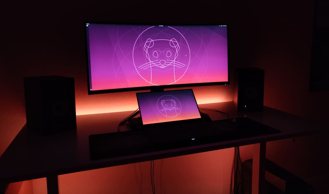 Illuminated desk with ultra-wide monitor and notebook.