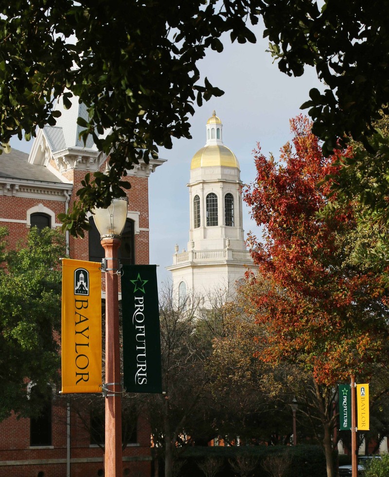 The gold steeple of Pat Neff Hall seen in the background of a Baylor University campus walkway