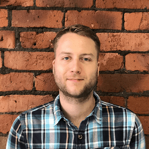 Dan Furze profile photo, wearing a blue checked shirt against an exposed brick wall.