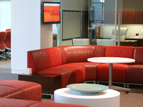 Sophisticated shared workspace with red leather style corner sofa and round white tables in front of glass wall office Zoom background