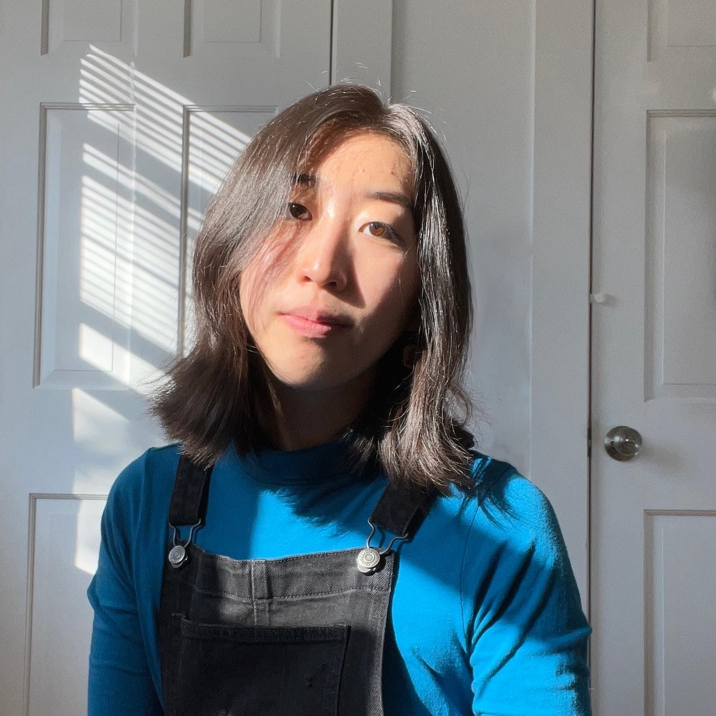 a picture of Angelina Han, an Asian woman with short brown hair, wearing a teal turtleneck and black overalls.