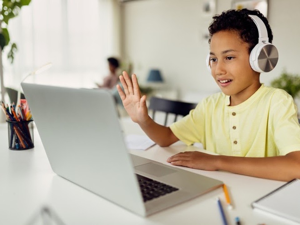 An online student waves to their teacher through their laptop