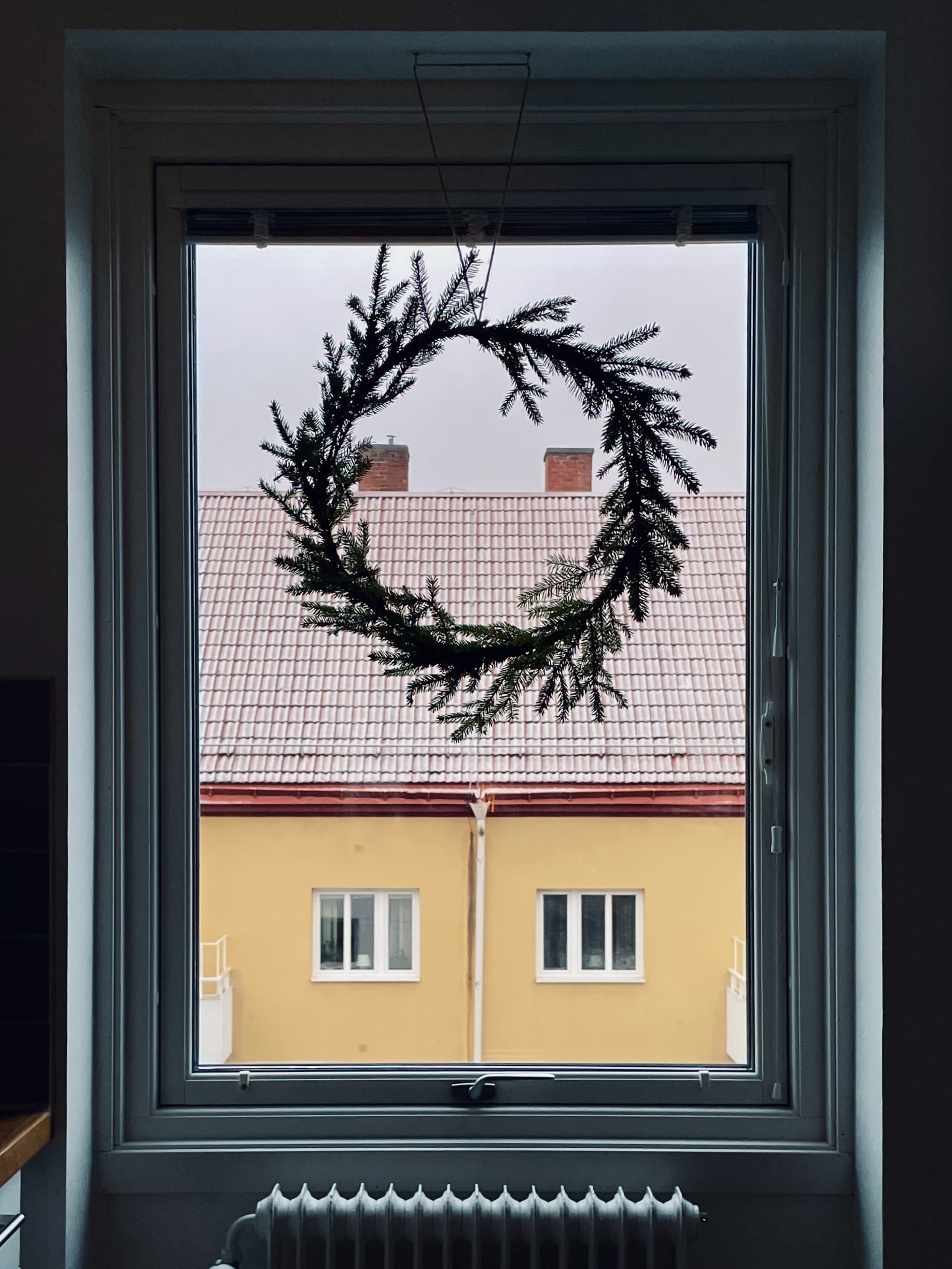 A silhouette of a wreath tied with spruce twigs is hanging in a window.