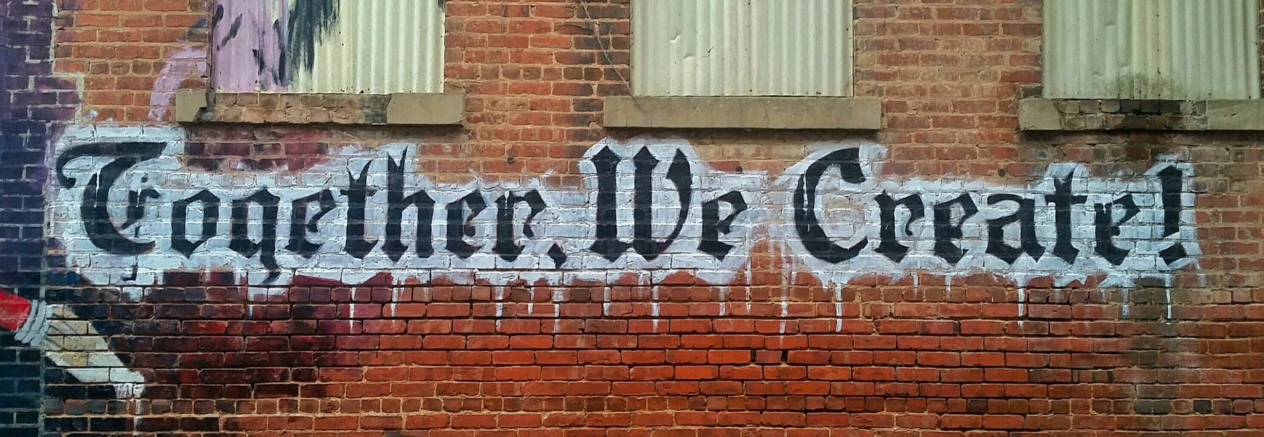Graffiti on a brick wall that says together we create.