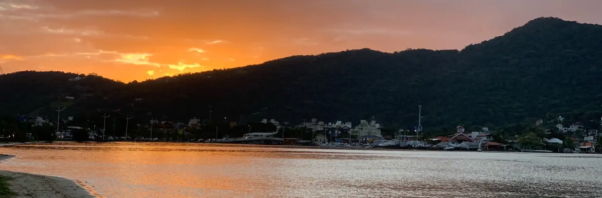 Por do sol com céu alaranjado por trás dos morros refletindo na água da lagoa