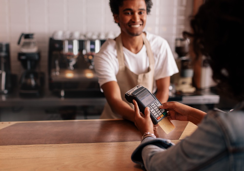 Cashier at local coffee house smiling and handing a card payment reader to a woman customer