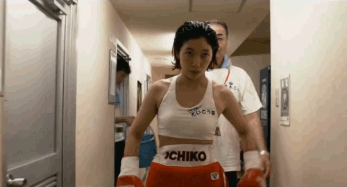 An animated gif of a scene from the film '100 Yen Love' of Ichiko in boxing gloves walking towards the camera punching her fists together.