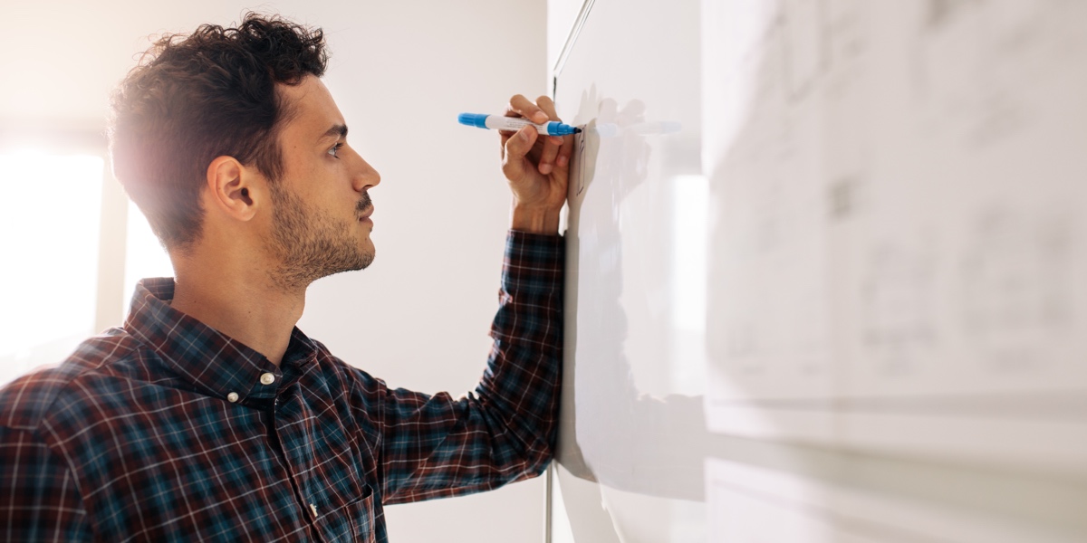 UX Whiteboard Design Challenge: The Ultimate Guide Designer standing at a whiteboard with a blue marker in hand.