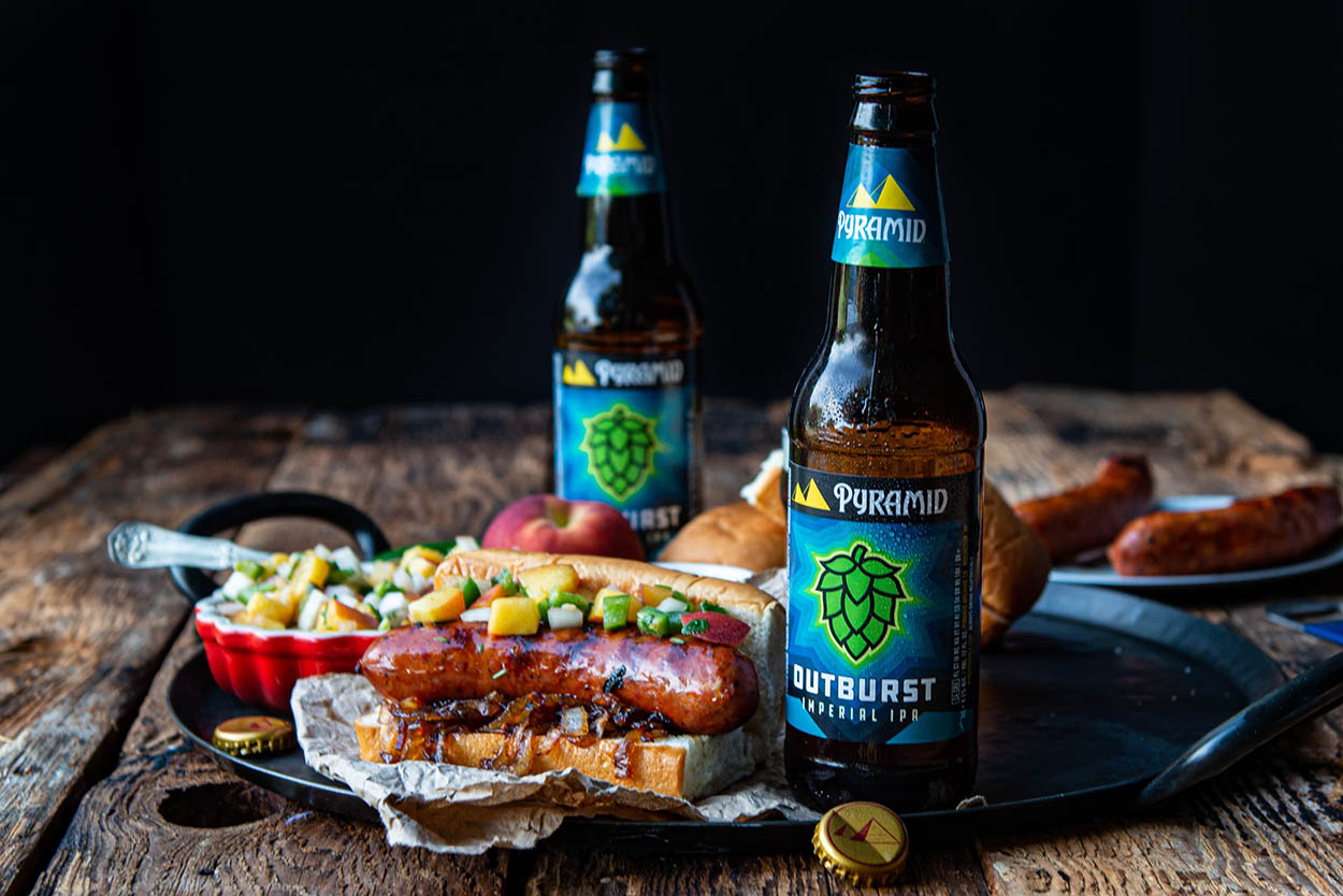 Bratwursts cooked in IPA beer with spicy homemade peach salsa a photo of delicious homecooked bratwurst served with spicy homemade peach salsa and topped with carmelized onions, all served with a cold bottle of Outburst IPA
