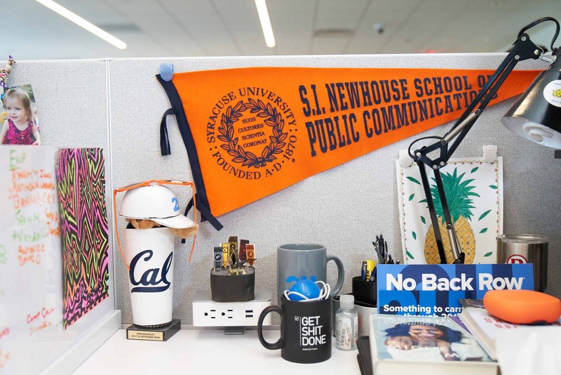 A 2U employee's desk with a Syracuse pennant, Cal University cup, and other novelty items