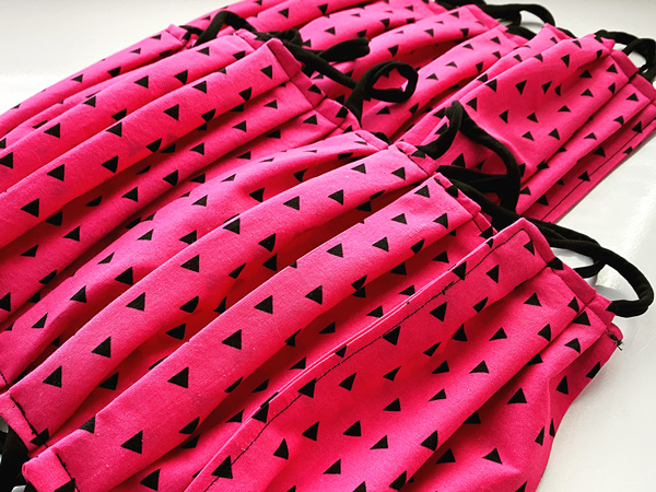 A pile of masks made from hot pink fabric with black triangles on it