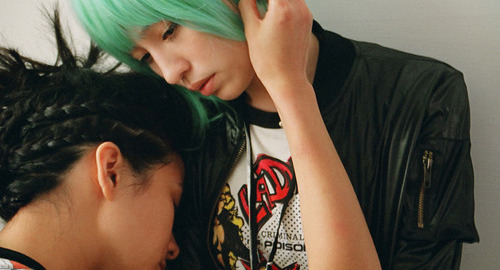 A close-up screenshot from the movie 'Candy Rain' of a young woman with braided hair embracing another woman with light-teal hair.