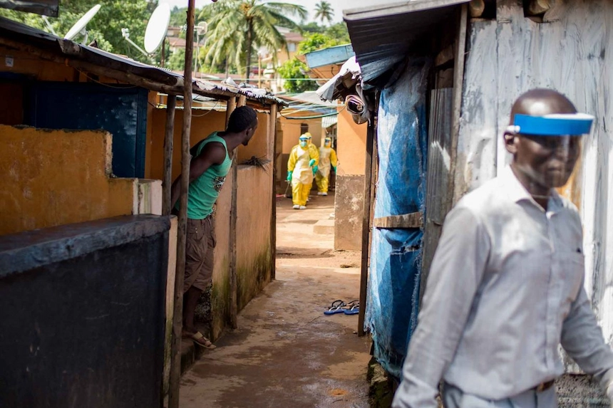 A resident watches a Concern Worldwide Burial Team walk through the alleys of Freetown, during the Ebola outbreak.