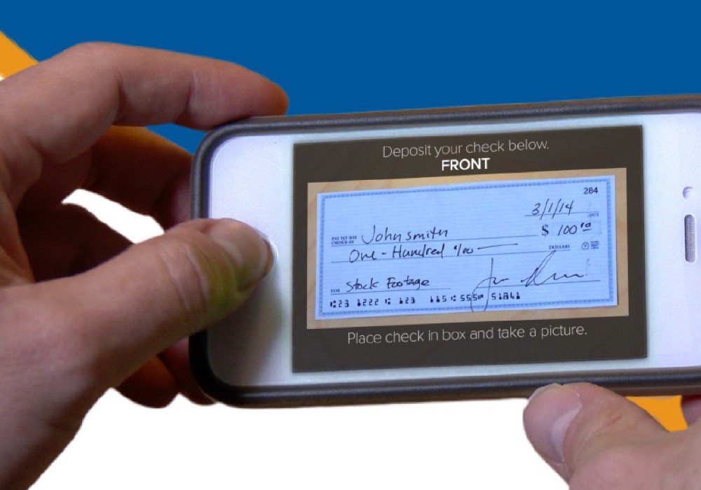 Two hands holding a smartphone. The image on the screen of the smartphone shows the front of a check as if the phone just took a picture of the check.