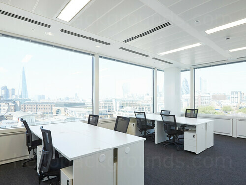 Spacious shared workspace featuring white desks with black office chairs and windows offering London city skyline view   Skype background