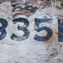 A cropped phone number painted in a copperplate font onto a flaking brick wall. The digits spell thirty five.