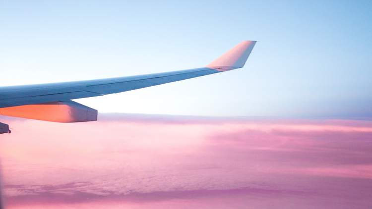 An image of a plane wing above the clouds at sunset