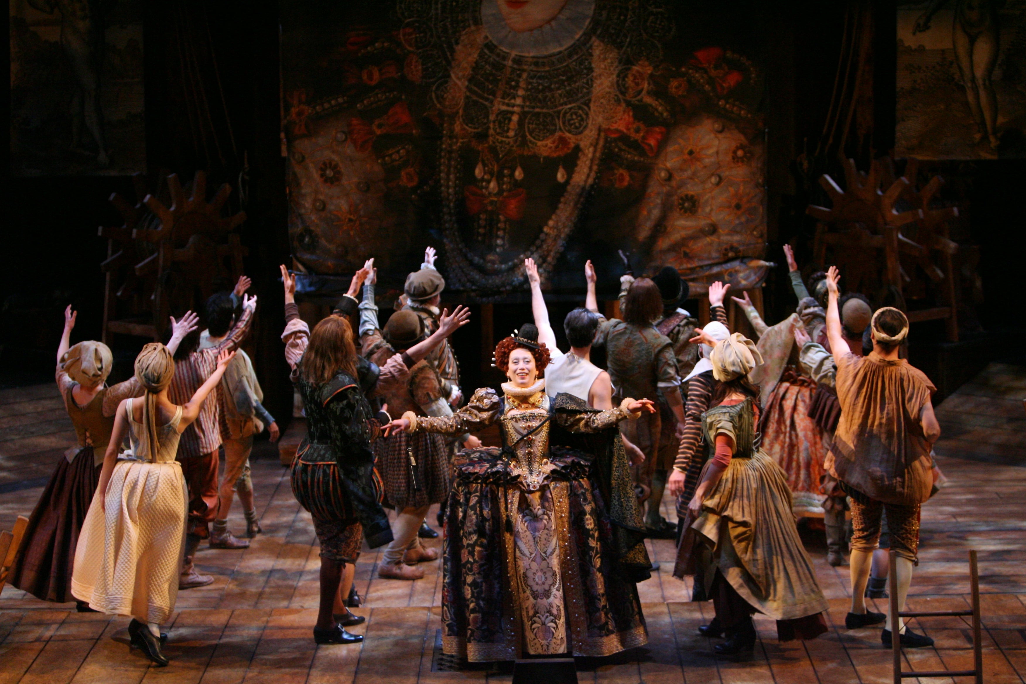 Queen Elizabeth I dances with a company of theatre players saluting her giant portrait in the background.
