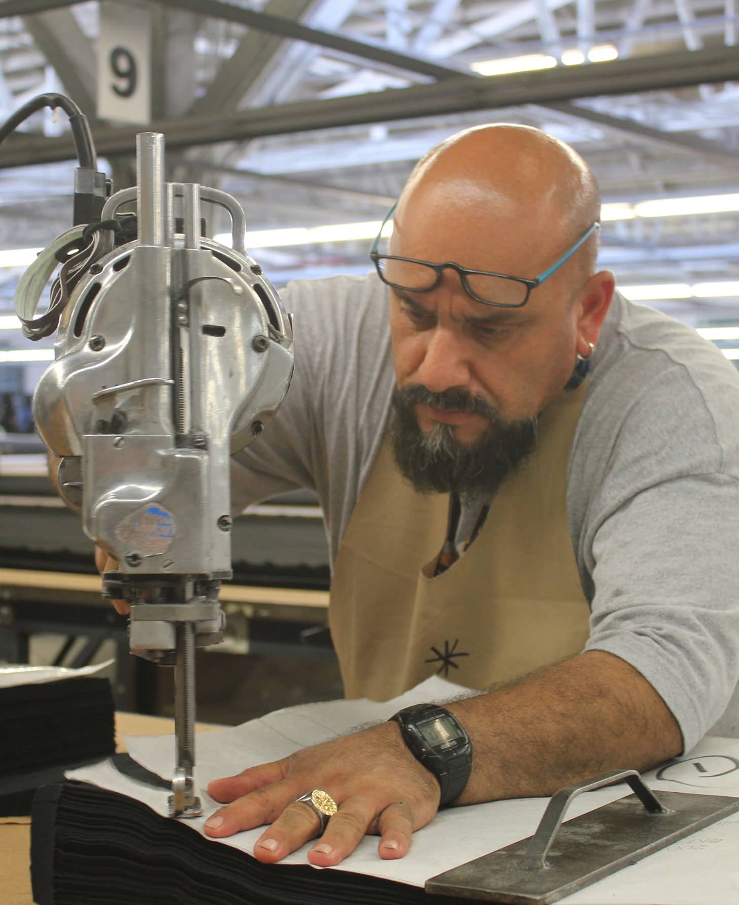 Man with glasses using a straight knife cutting machine to cut fabric